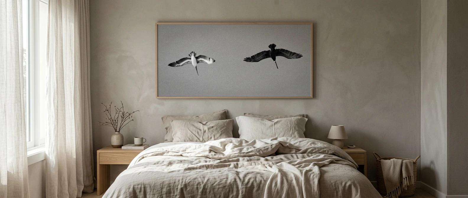 A calm monochrome bedroom in soft warm greys and off-white: a rumpled oatmeal linen bed beneath one oversized, muted charcoal-and-cream abstract print with a pale arch, in a thin pale oak frame, lit by soft morning window light. please include the referenced image as the wall art.